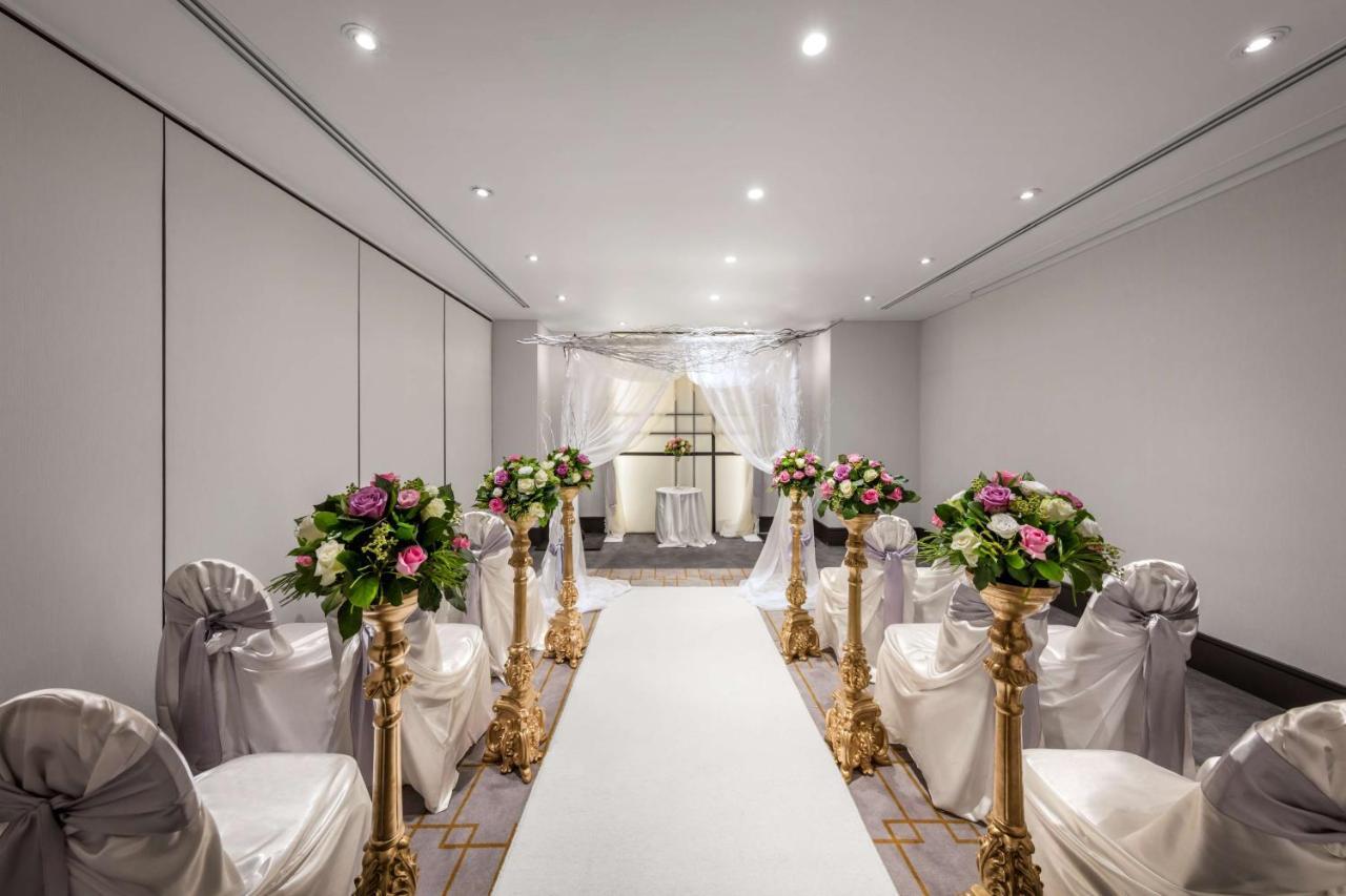 Radisson Blu Plaza Hotel Sydney Exterior photo The photo shows a beautifully arranged indoor event space, likely set up for a wedding ceremony. There is a long white aisle runner leading to a decorated archway at the end. On either side of the aisle, there are elegant chairs draped in white fabri